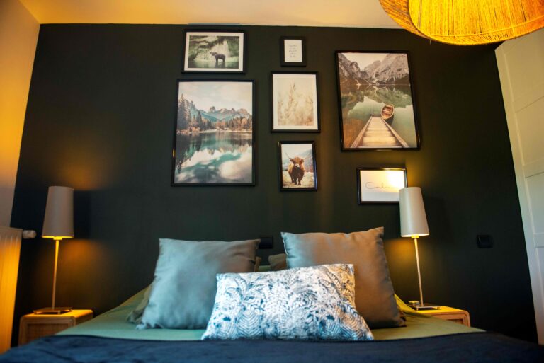 Vue frontale du lit dans le projet Dressing chic conçu par Bulle Intérieure, avec coussins décoratifs, mur foncé à cadres et lampes symétriques