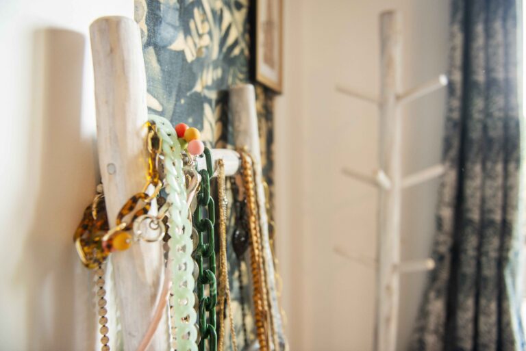 Détail du projet Dressing chic par Bulle Intérieure : bijoux colorés accrochés sur un porte-accessoires en bois, devant un papier peint végétal