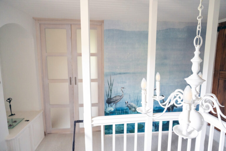 Vue sur la double porte battante vitrée et la tapisserie panoramique bleue marquant l’entrée de la suite parentale dans une maison rénovée à Saint-Nizier-du-Moucherotte.