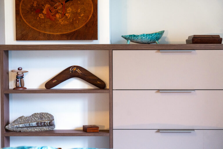 Mobilier sur-mesure dans une chambre rénovée, avec dressing à portes coulissantes, commode intégrée et grille en métal perforé pour le conduit de cheminée.