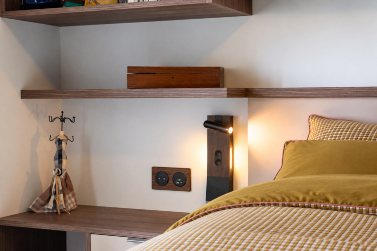 Détail d'un chevet sur mesure en bois avec liseuse orientable, éclairage intégré, prise électrique et ports USB dans une chambre du Vercors.