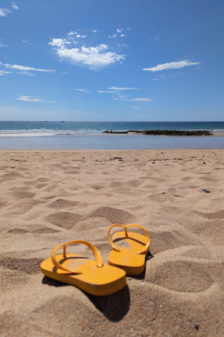 Paire de tongs jaunes posées sur le sable d’une plage bretonne avec vue sur la mer et l’horizon bleu.