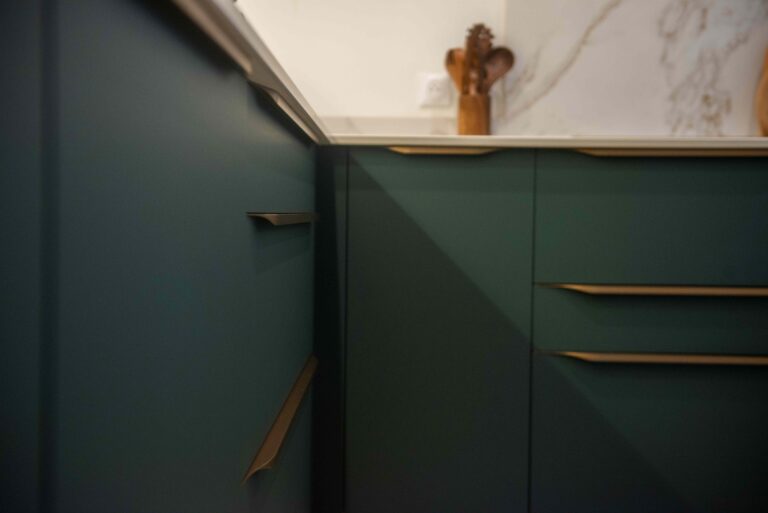Gros plan sur les poignées dorées des tiroirs vert émeraude dans une cuisine contemporaine