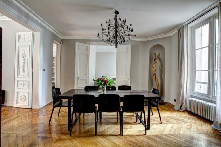 Intérieur haussmannien rénové avec parquet point de Hongrie, moulures, grande table et double porte en enfilade.