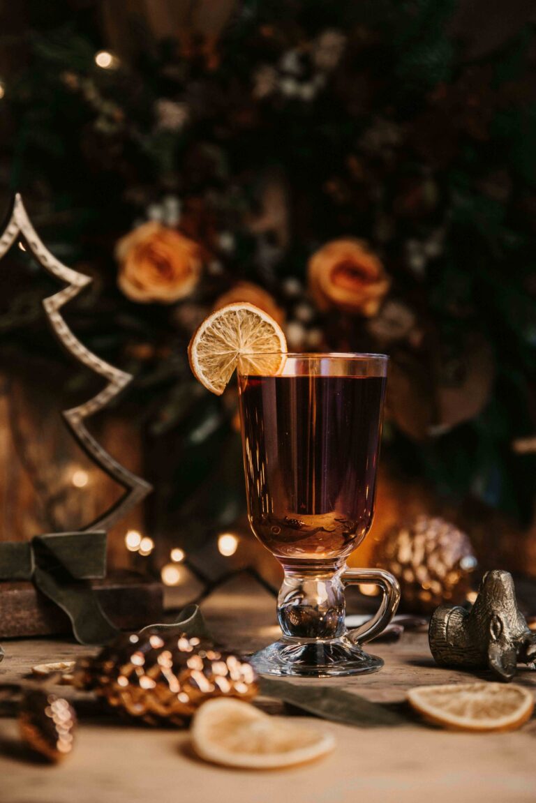 Verre de boisson chaude avec une tranche d’orange posé sur une table décorée pour Noël, entouré d’éléments naturels et lumineux.